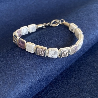 Pulseira com contas quadradas brancas, lilás e prateadas com fecho metálico em fundo azul