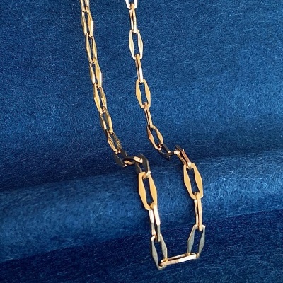 Corrente dourada com elos alongados sobre fundo azul texturizado