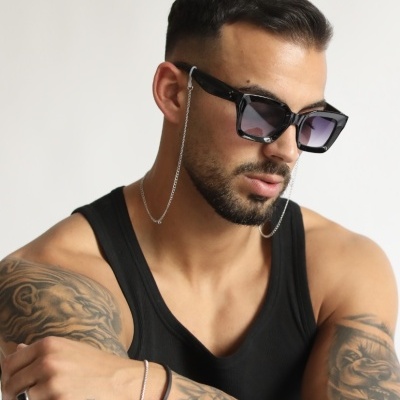 Homem com óculos de sol pretos, camisola preta e tatuagens nos braços