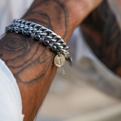 Pulseira masculina de aço inoxidável com pendente num pulso tatuado