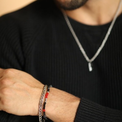 Homem com camisola preta e pulseiras prateadas com contas vermelhas, pretas e transparentes no pulso esquerdo.