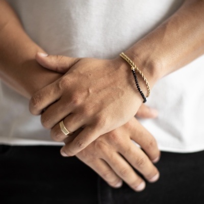 Mãos com pulseira dourada, pulseira preta e anel dourado com camiseta branca