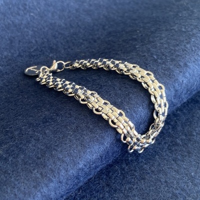 Pulseira dourada entrelaçada sobre fundo de tecido azul