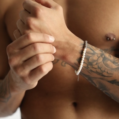 Pulseira de contas brancas em pulso de homem tatuado e sem camisa