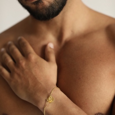 Pulseira dourada com pendente no pulso de homem sem camisa