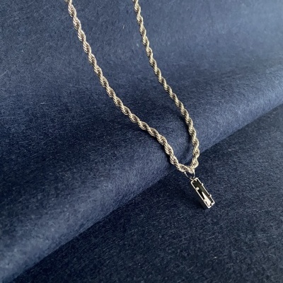 Colar dourado com corrente trançada e pendente retangular sobre fundo azul escuro