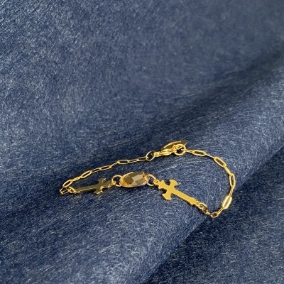 Pulseira dourada com cruzes e pendente oval sobre tecido azul escuro