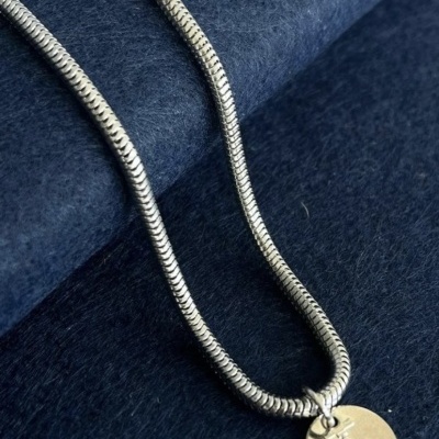 Colar prateado com pendente redondo e âncora gravada sobre tecido azul escuro