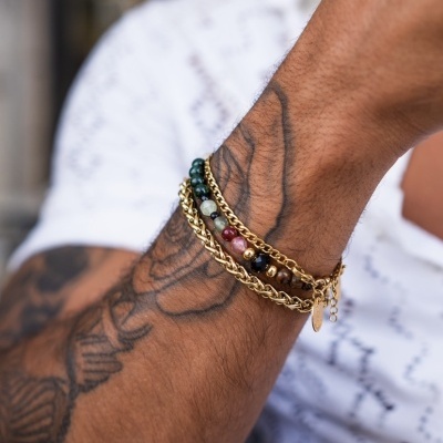 Pulseira dourada e com contas coloridas no pulso de um homem tatuado