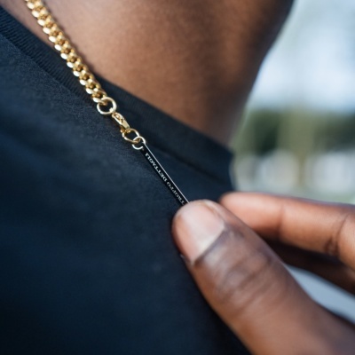 Colar dourado com etiqueta preta e texto PRMZ MUSEUM num pescoço