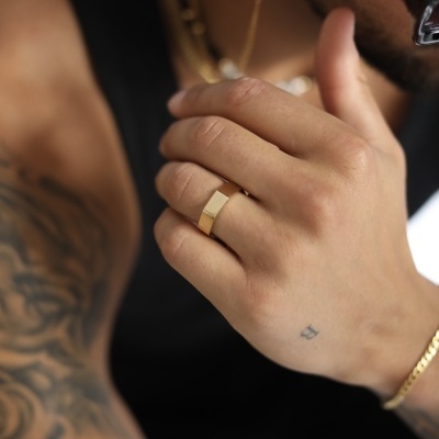 Homem com anel e pulseira dourados e tatuagens no braço esquerdo vestido com camisa preta