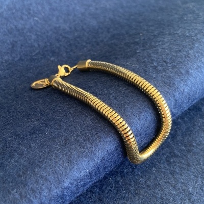 Pulseira dourada com fecho e pendente sobre fundo azul