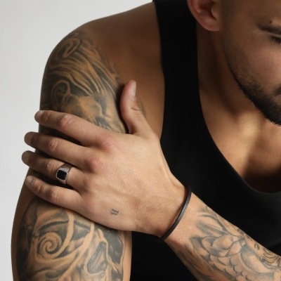 Braço tatuado masculino com anel e pulseira a vestir camisola preta