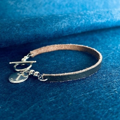 pulseira de pele castanha com fecho e pendente metálicos sobre tecido azul