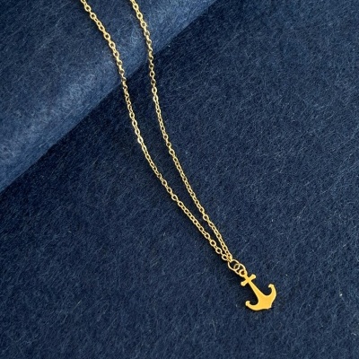 Colar dourado com pendente de âncora sobre tecido azul