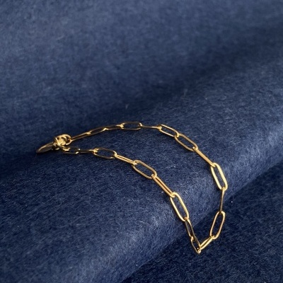 Pulseira dourada de elos alongados sobre tecido azul escuro