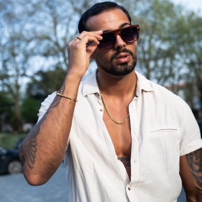 Homem com óculos de sol castanhos e camisa branca em ambiente exterior