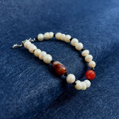 Pulseira com contas brancas, castanhas e vermelhas sobre superfície azul escura