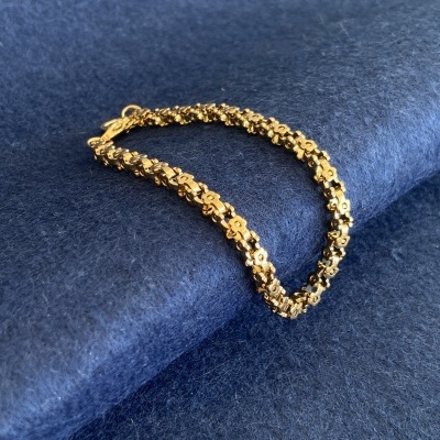 Pulseira dourada com elos de flores sobre fundo azul felpudo
