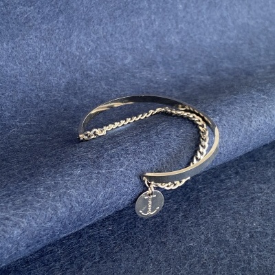 Pulseira prateada com pendente J sobre tecido azul