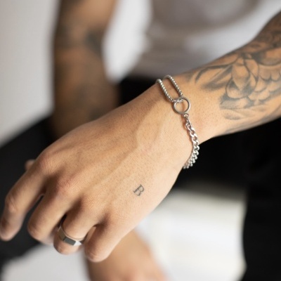 Pulseira de metal prateado em pulso com tatuagens e anel