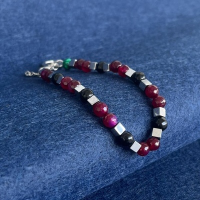 Pulseira com contas vermelhas, negras e prateadas sobre fundo azul