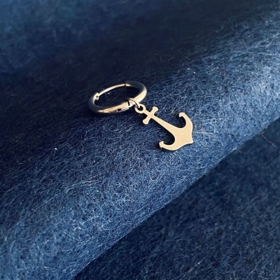 Brinco prateado com pendente de âncora sobre tecido azul