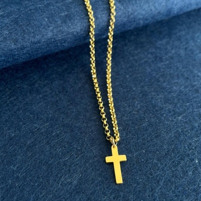 Colar dourado com pendente em forma de cruz sobre fundo azul escuro