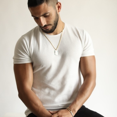 Homem com t-shirt branca e colar sentado com fundo branco