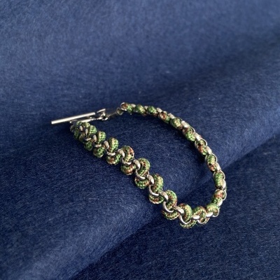 Pulseira entrelaçada verde e bege com fecho prateado sobre tecido azul escuro