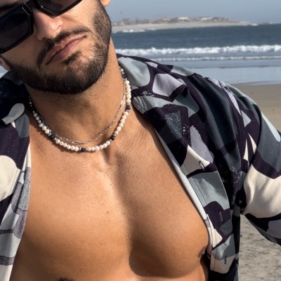 Homem na praia com óculos escuros, colares e camisa geométrica aberta