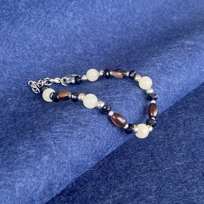 Pulseira de contas brancas, castanhas, pretas e prateadas sobre tecido azul