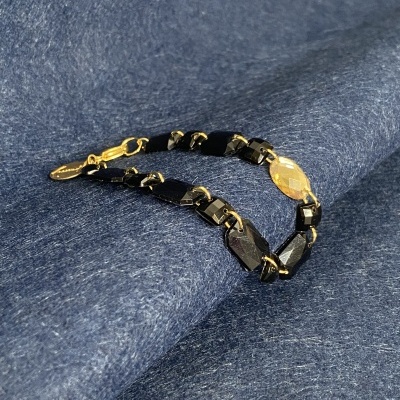 Pulseira preta com detalhes dourados sobre tecido azul.