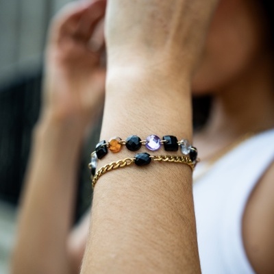 Pulseiras de contas e corrente dourada no pulso de uma pessoa com camisa branca