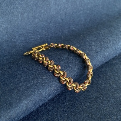 Pulseira entrelaçada dourada e castanha sobre tecido azul escuro