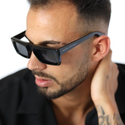 Óculos de sol pretos quadrados com texto na haste usados por um homem com tatuagens.