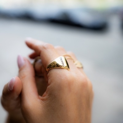 Anel dourado com a palavra J'adore no dedo de uma mão em ambiente exterior