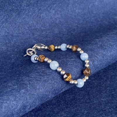 Pulseira com contas prateadas, castanhas e azuis sobre tecido azul
