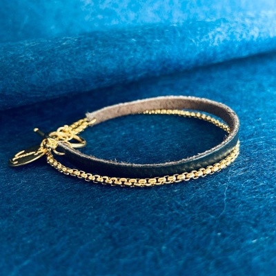 Pulseira de couro castanho com corrente dourada sobre fundo azul.