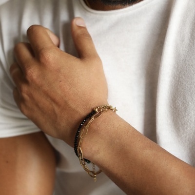 Homem usando pulseira com contas pretas e elos dourados no pulso