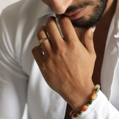 Homem com anel dourado e pulseira de contas em camisa branca