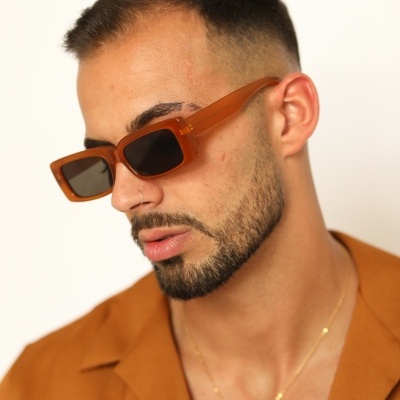 Homem com óculos de sol quadrados castanhos e camisa castanha.