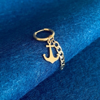 Argola dourada com pendente em forma de âncora e corrente sobre tecido azul