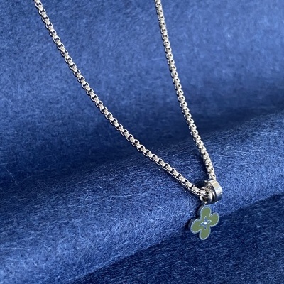 Colar prateado com pendente flor verde sobre fundo azul