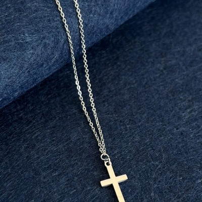 Colar prateado com pendente de cruz sobre tecido azul escuro