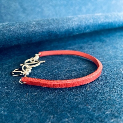 Pulseira vermelha fina com fecho prateado sobre superfície azul