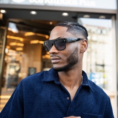 Homem com óculos de sol pretos e camisa azul em frente à loja