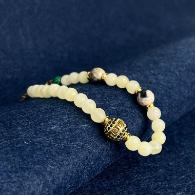 Pulseira de contas brancas, dourada e verdes sobre tecido azul