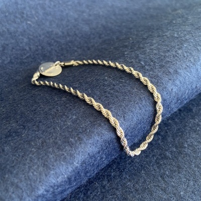 Pulseira com corrente torcida em metal prateado com medalha redonda em fundo azul escuro