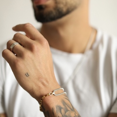 Mão masculina com pulseiras dourada e prateada, anel e tatuagens